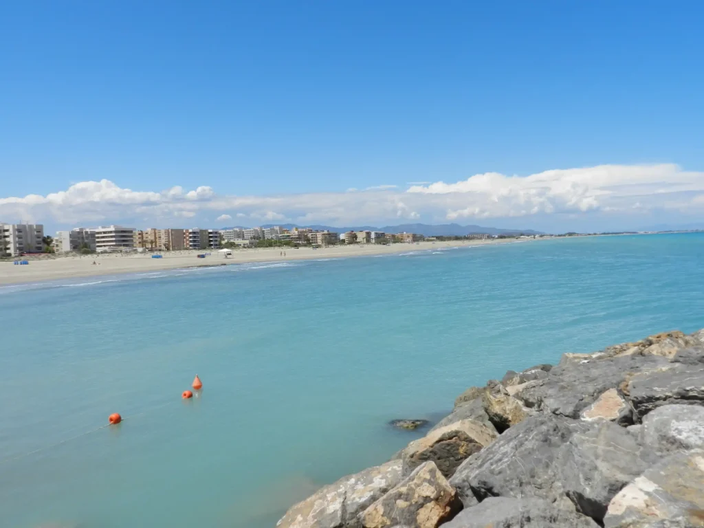Playa con edificios en el horizonte y rocas en primer plano