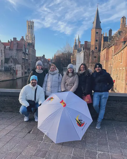 Grupo de personas posando junto a un paraguas en Brujas, con el Belfort al fondo.