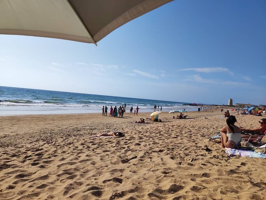Playa con sombrilla y personas disfrutando del sol en El Palmar.