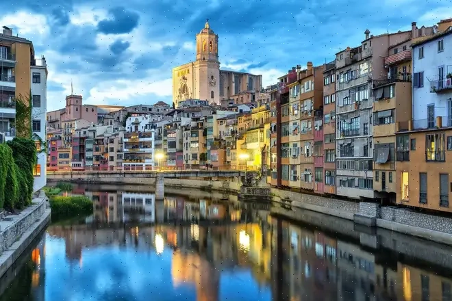Vista panorámica de Girona con edificios históricos y el río Onyar reflejado.