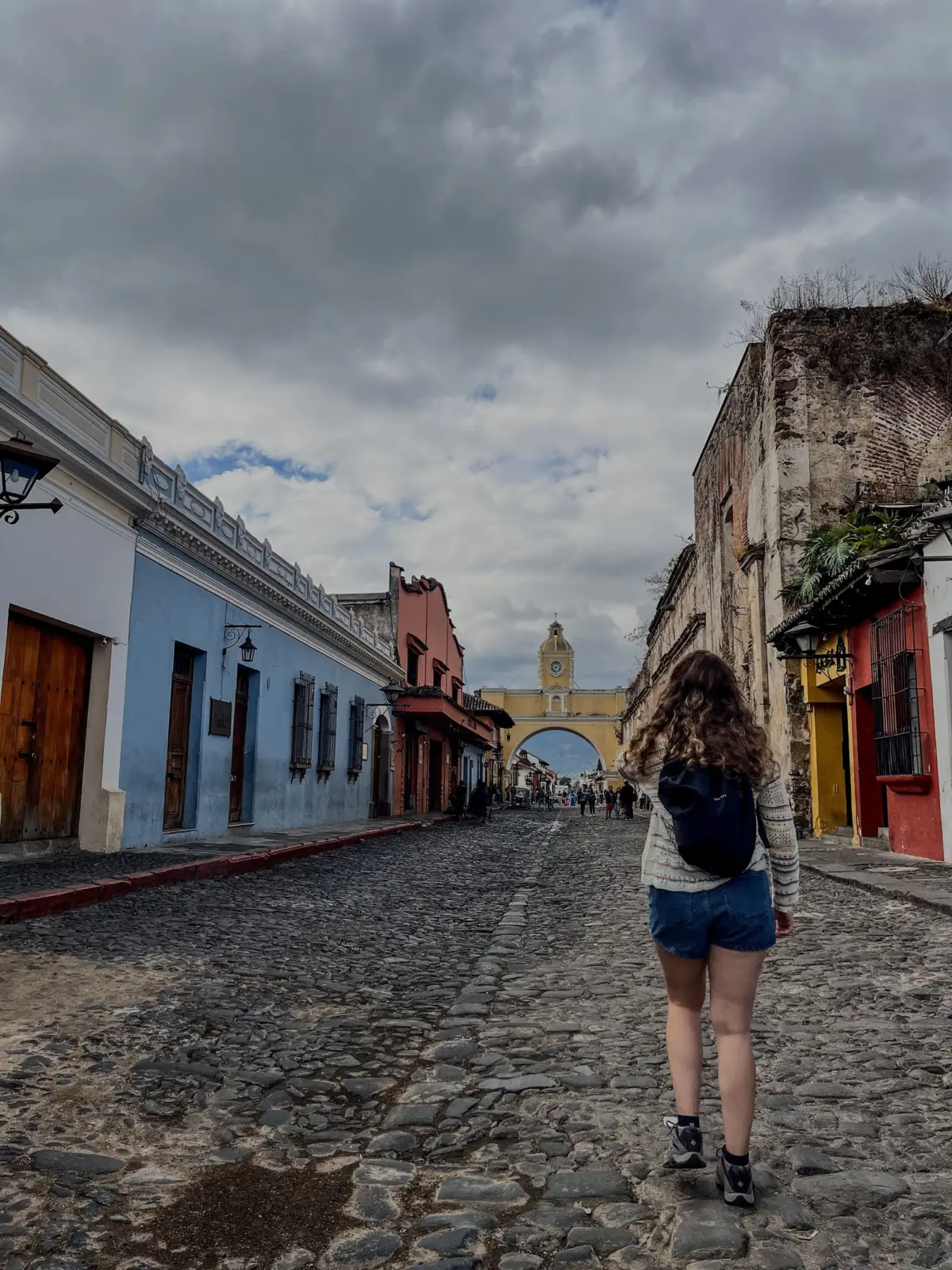 Traveller walking along a cobblestone street toward the Santa Catalina Arch in Antigua Guatemala