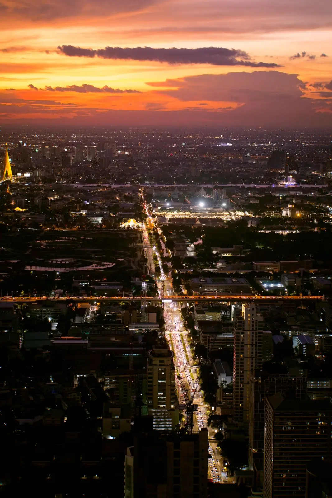 Vista aérea de Bangkok al anochecer con una avenida iluminada bajo el cielo naranja