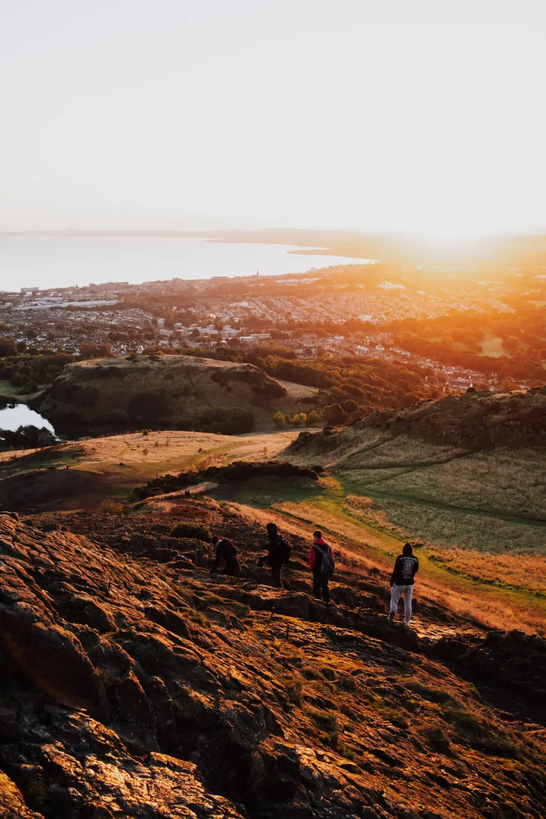 Hikers climbing the rocky slopes of Arthur’s Seat above Edinburgh at sunset