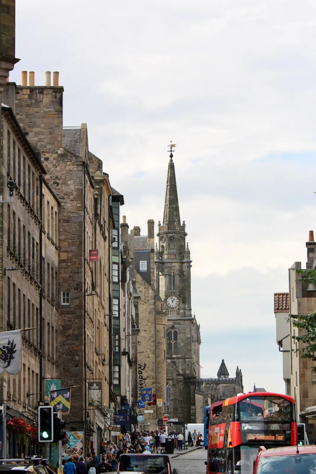 Pedestrians and a red sightseeing bus on Edinburgh’s Royal Mile, with the Tron Kirk spire ahead