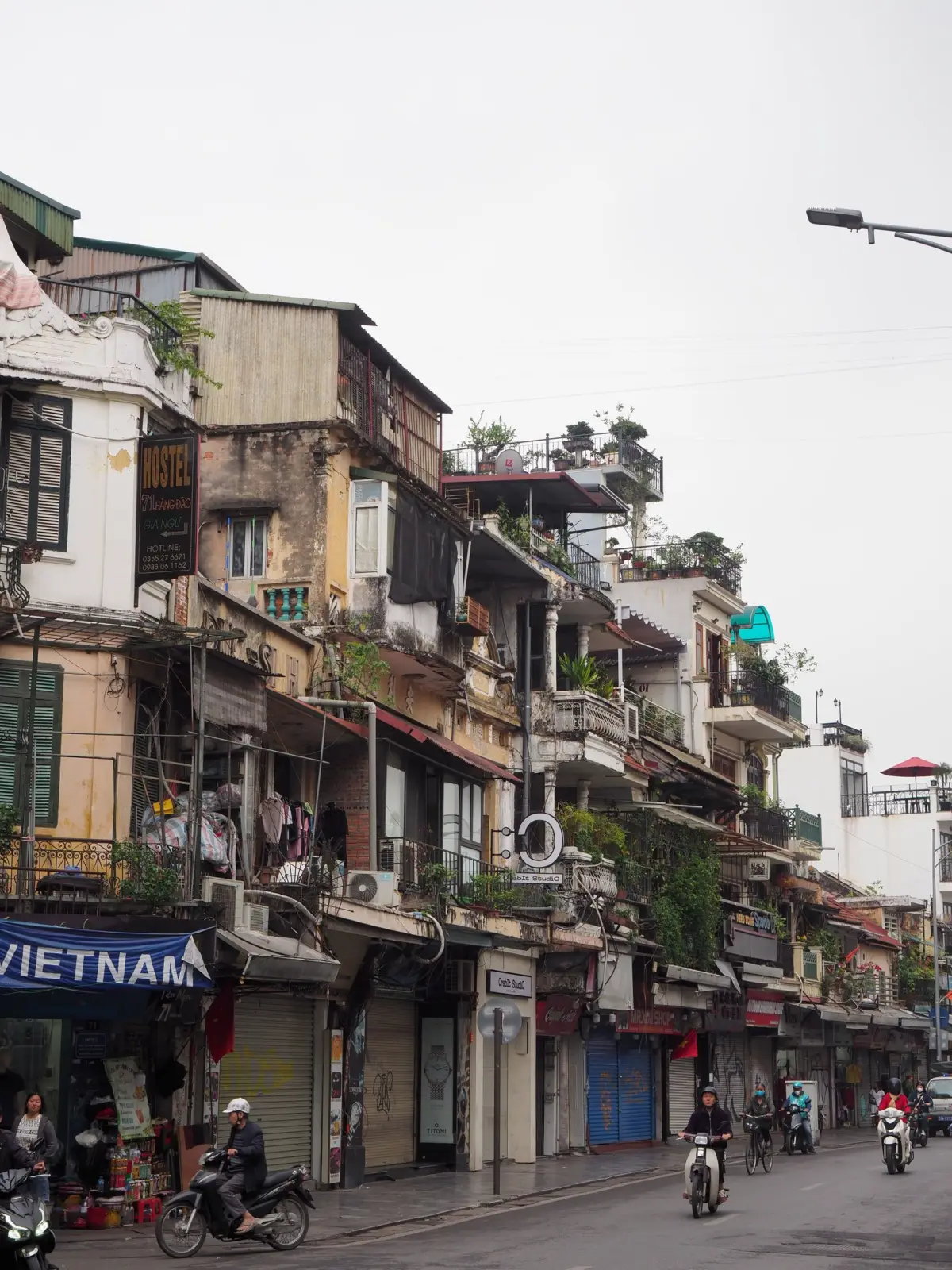 Calle comercial del casco antiguo de Hanói con casas estrechas, motos y peatones
