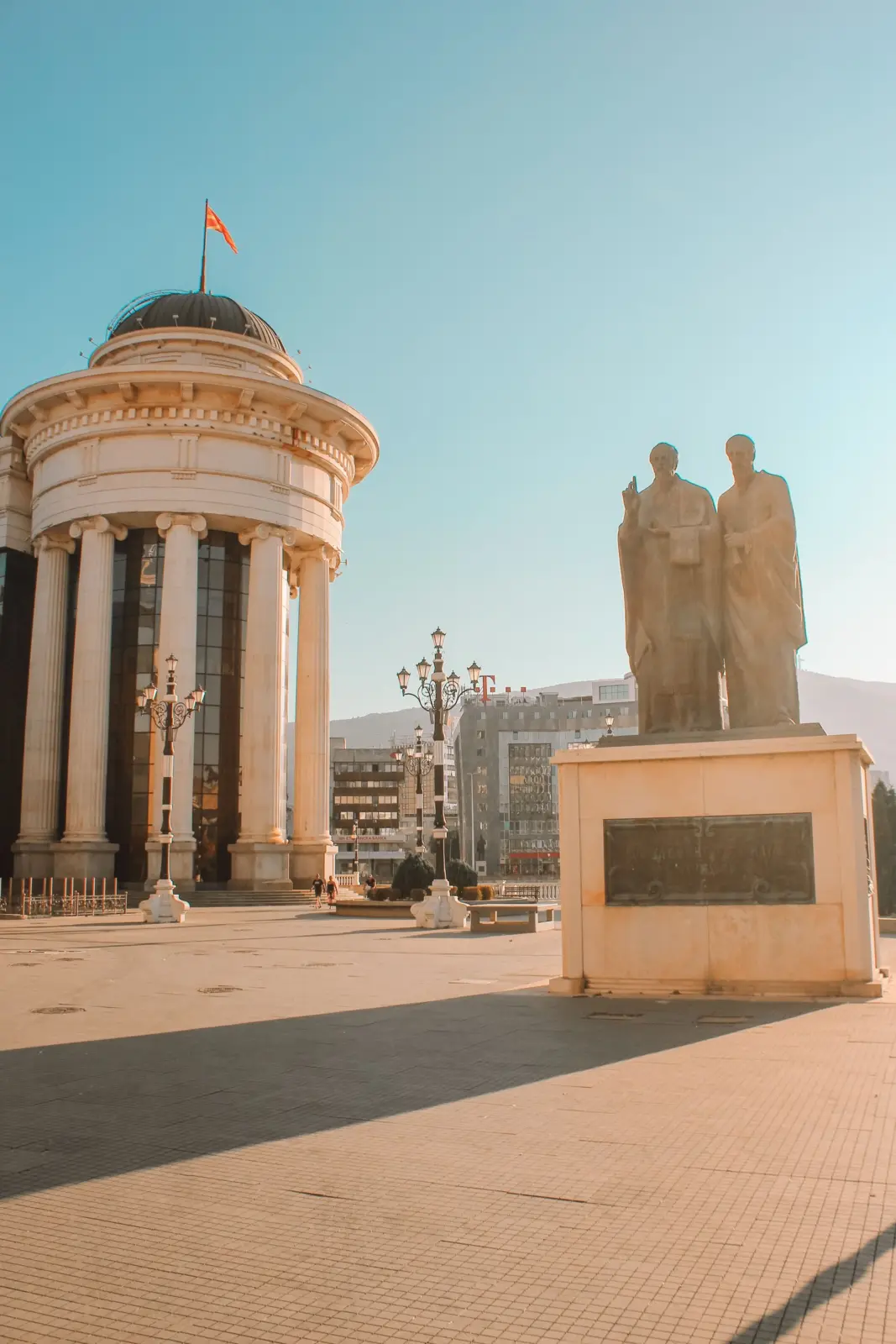 Edificio neoclásico y monumento con dos figuras en una plaza de Skopje