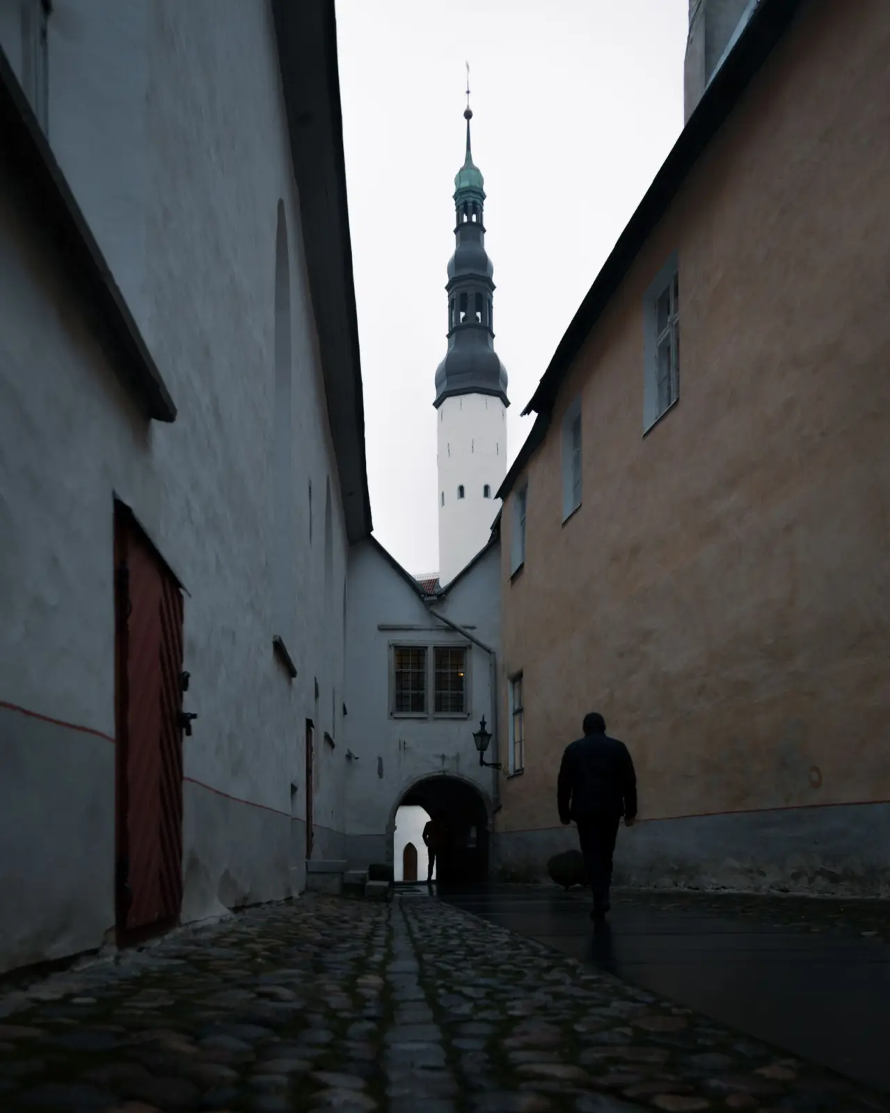 Peatones por una calle empedrada del casco antiguo de Tallin, con una torre al fondo