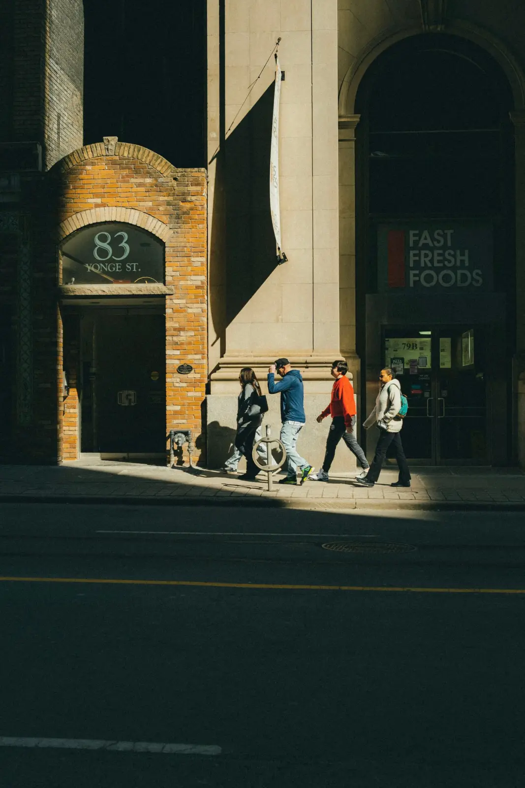Four pedestrians walking past 83 Yonge Street in Toronto