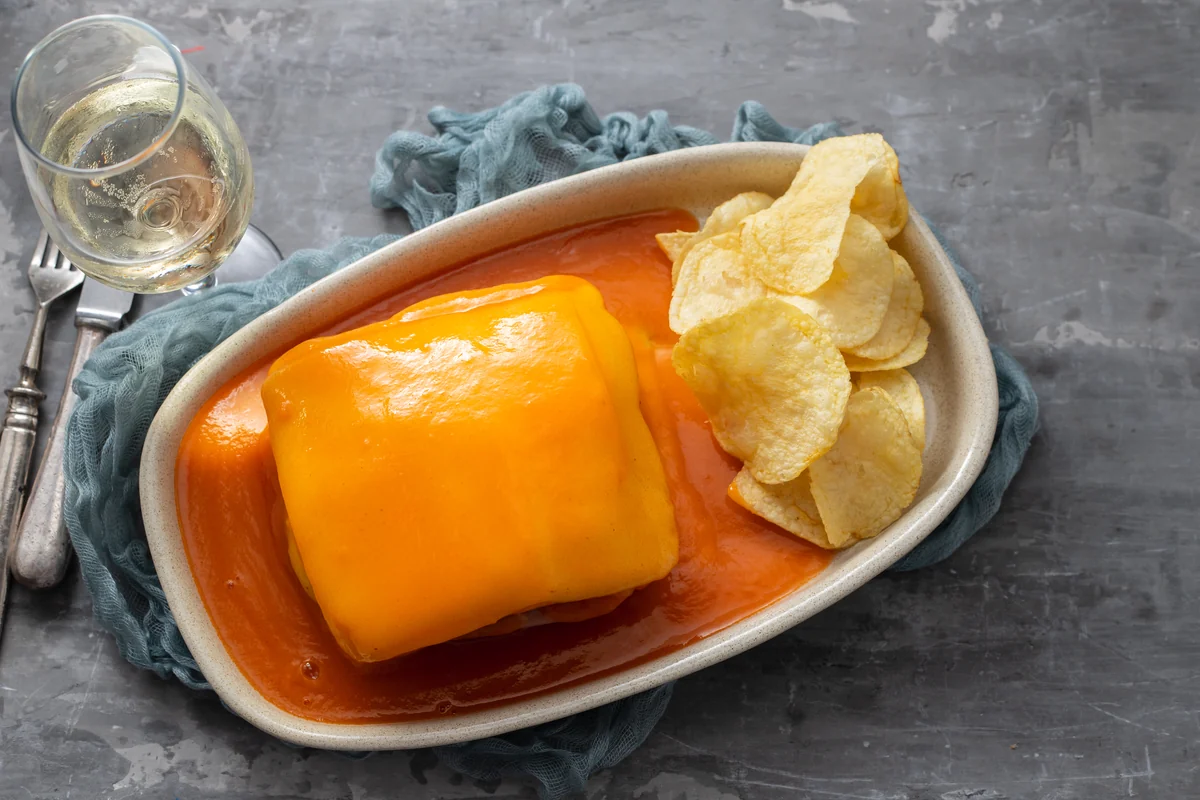 A francesinha covered in melted cheese and sauce, served with crisps