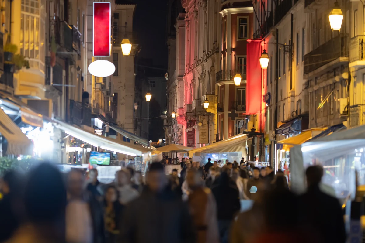 A crowded Lisbon street at night, lit by bar signs and street lamps