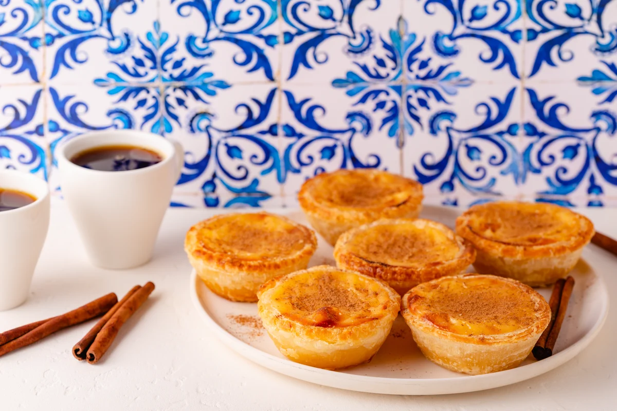 Pastéis de nata dusted with cinnamon and two cups of coffee against blue azulejo tiles