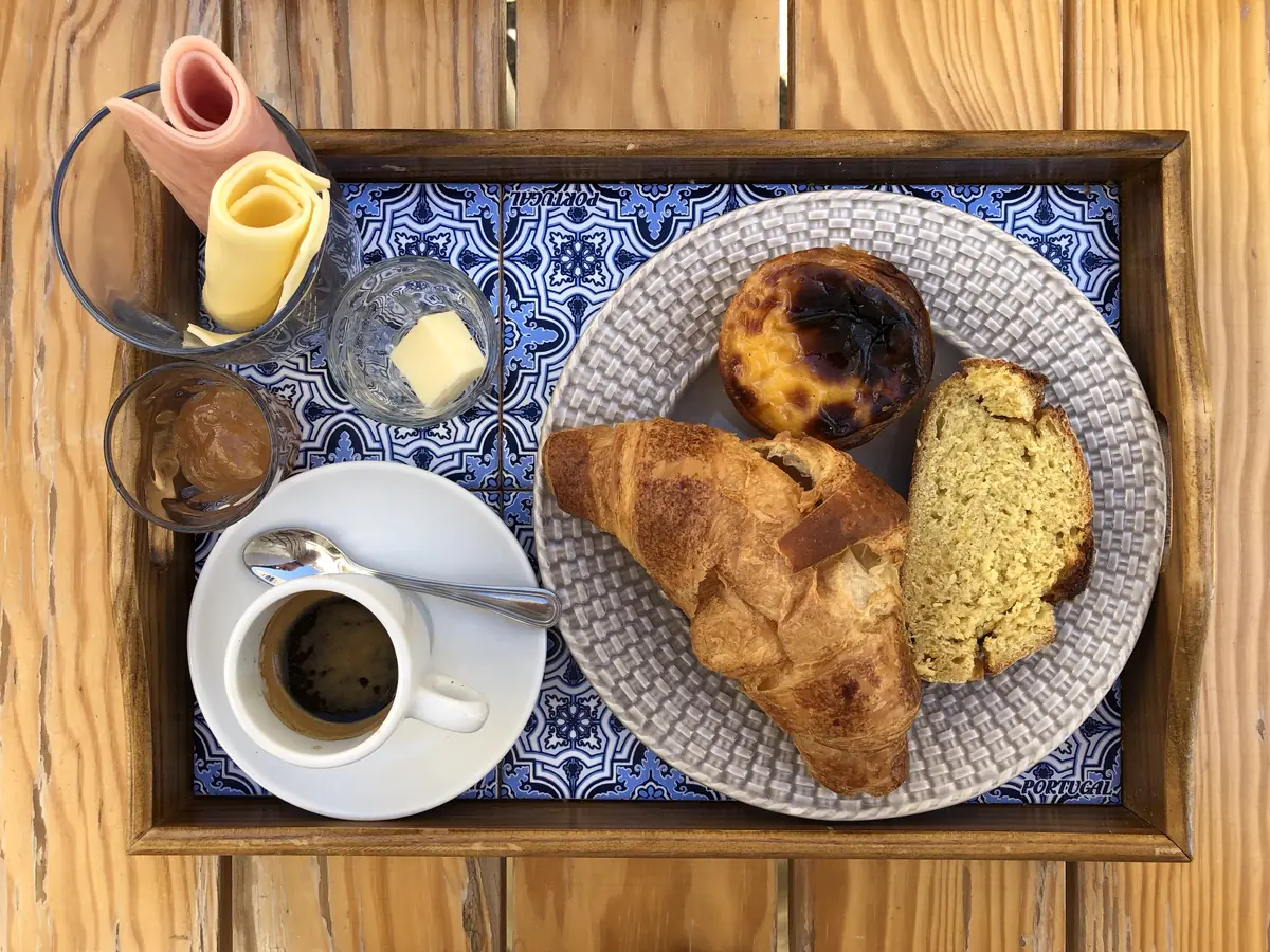 A breakfast tray with coffee, croissant, pastel de nata and bread on azulejo tiles